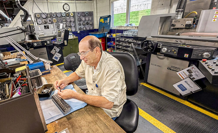 Manufacturing employee seated at a workbench inspecting small machined components inside the Ripley Tools production facility, surrounded by machining equipment and tooling.